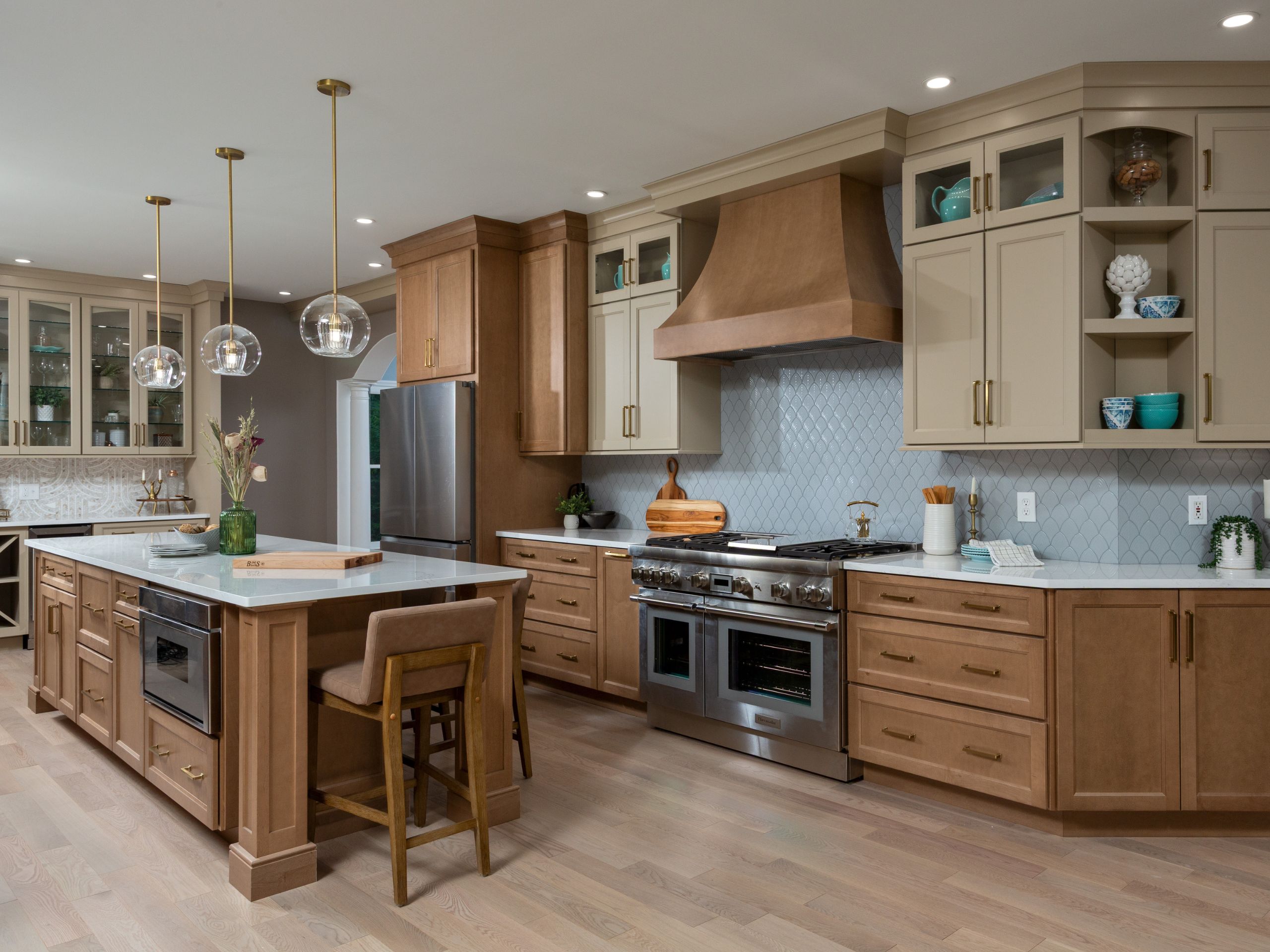 Transitional kitchen remodel with large island, wood cabinetry, cream upper cabinets, custom wood range hood, and glass pendant lighting
